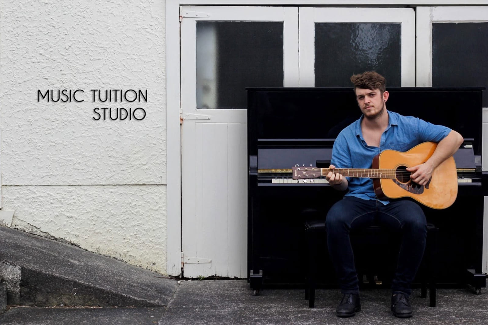 Adam Whybro with an acoustic guitar, sitting at an upright piano